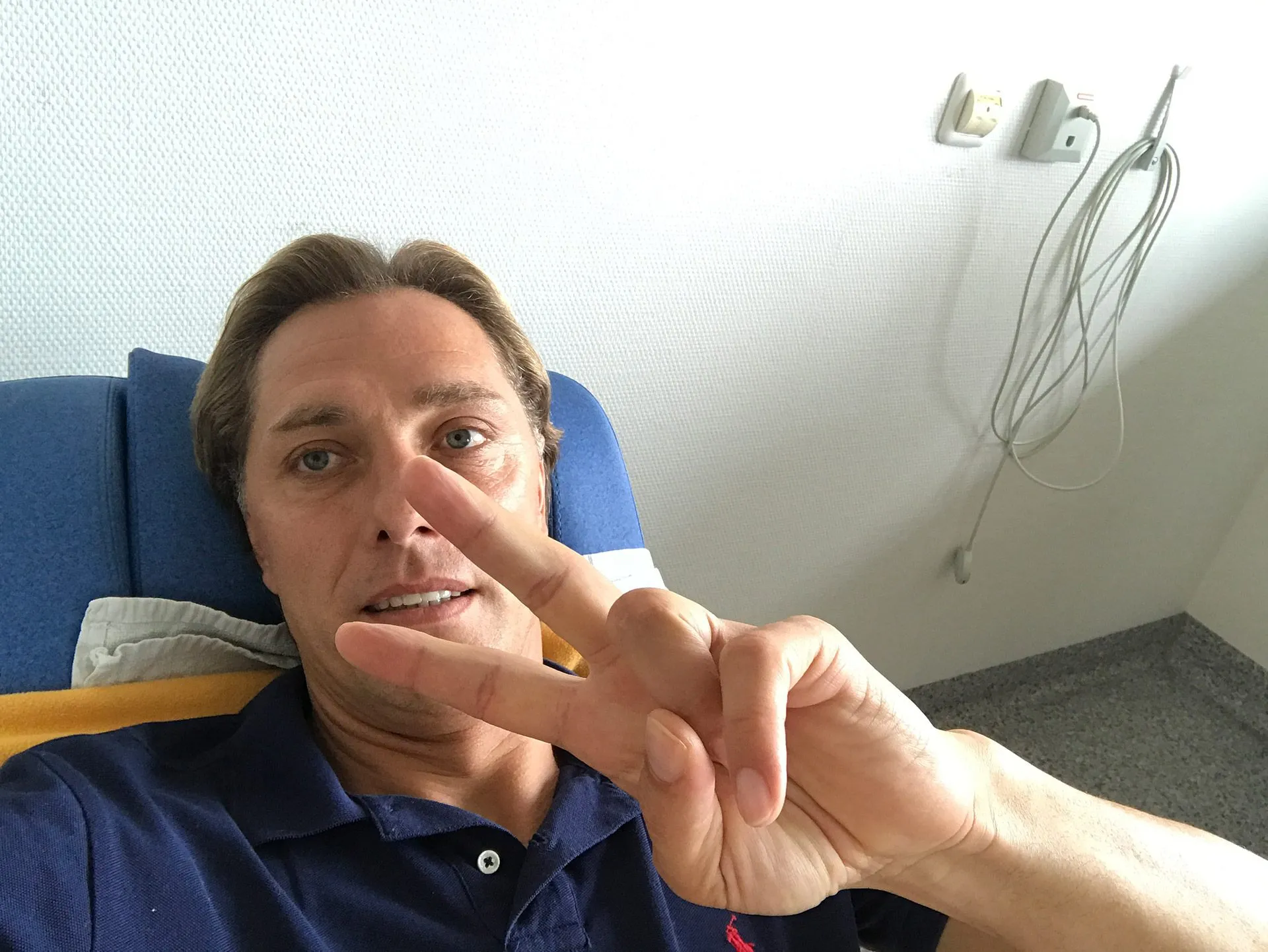 René Müller im Krankenhausbett zeigt lächelnd das Victory-Zeichen