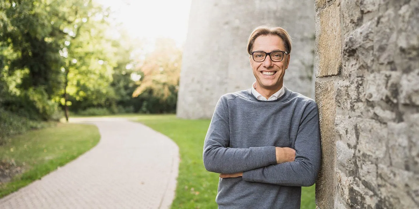 René Müller lehnt lächelnd mit verschränkten Armen an einer Mauer