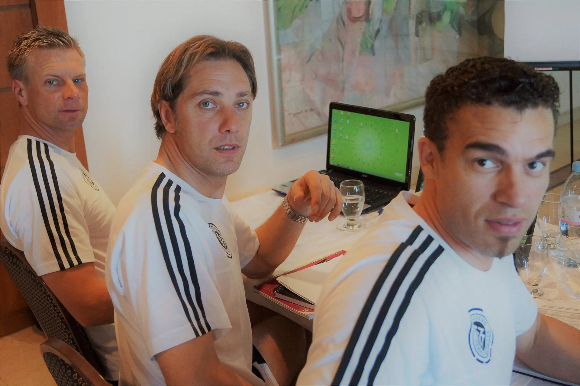 René Müller mit zwei Kollegen im Trainingsanzug an einem Schreibtisch